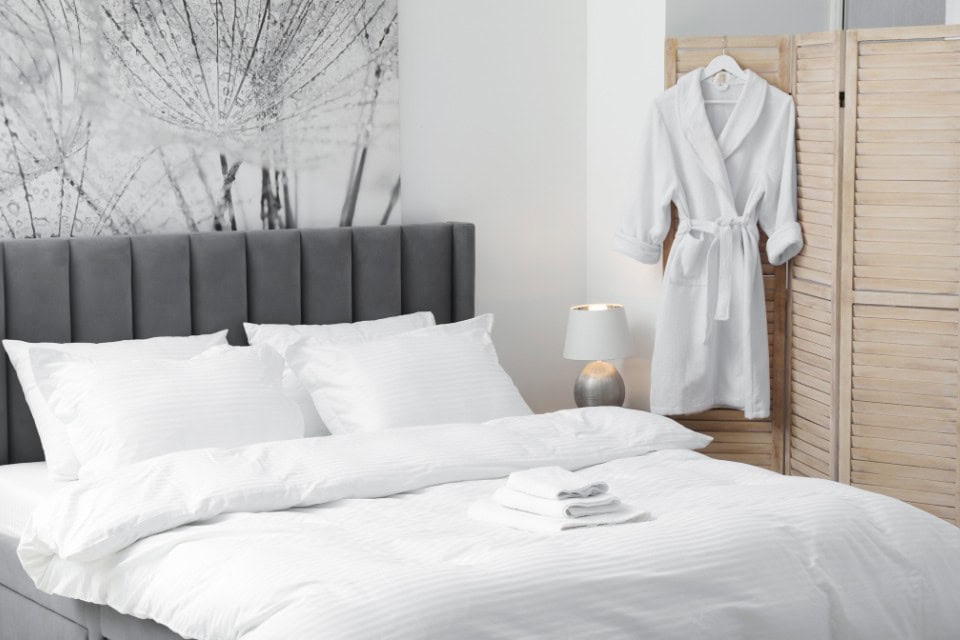 Pristine white linens and folded towels on a guest bed, prepared with Drop & Dash’s professional commercial laundry service for a hospitality business.