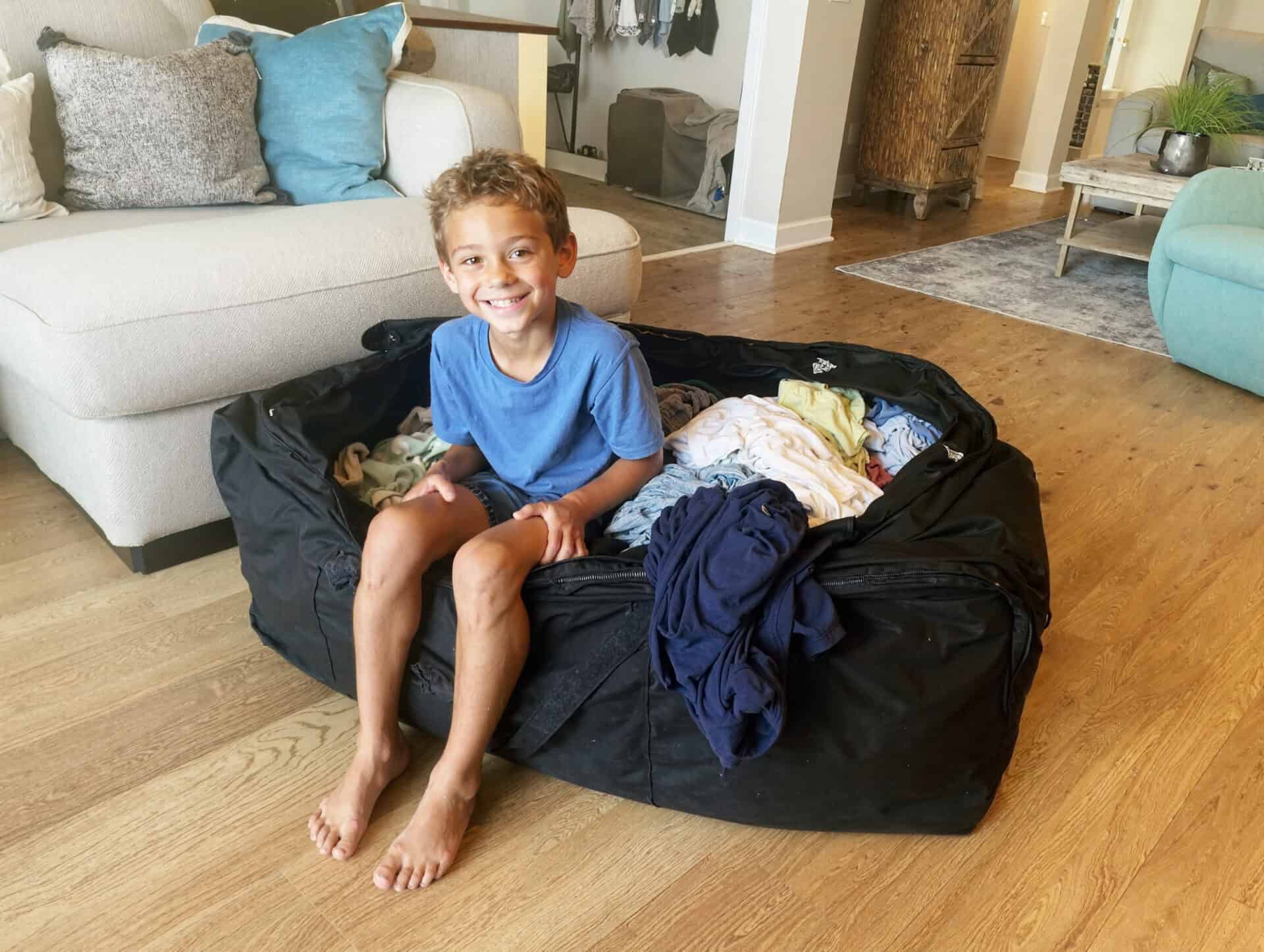 Smiling child sitting in large laundry bag indoors.