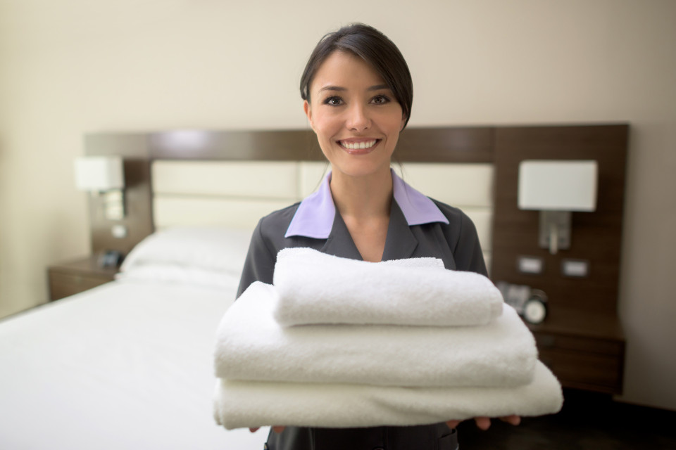 Smiling hotel staff holding freshly cleaned towels in a guest room, representing Drop & Dash hotel linen cleaning service in Chicago