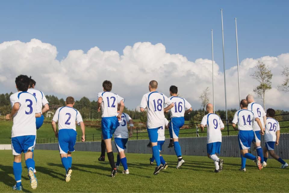 Soccer team in blue and white uniforms jogging together on a field during practice