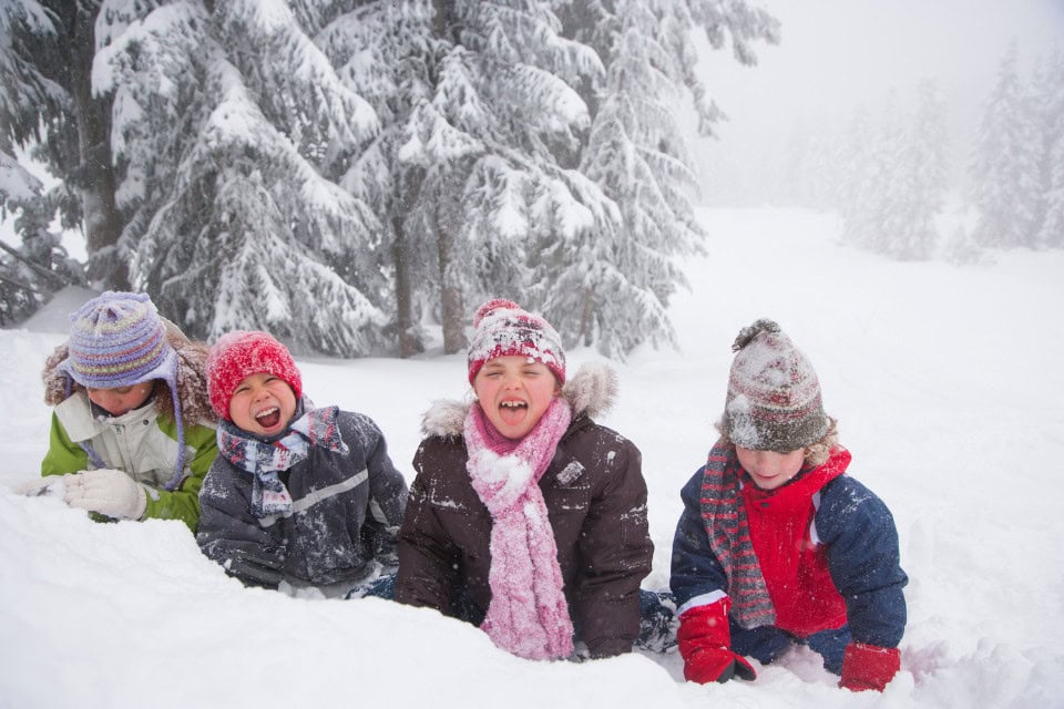 Children bundled in winter coats, scarves, and hats playing in the snow on a snowy day.